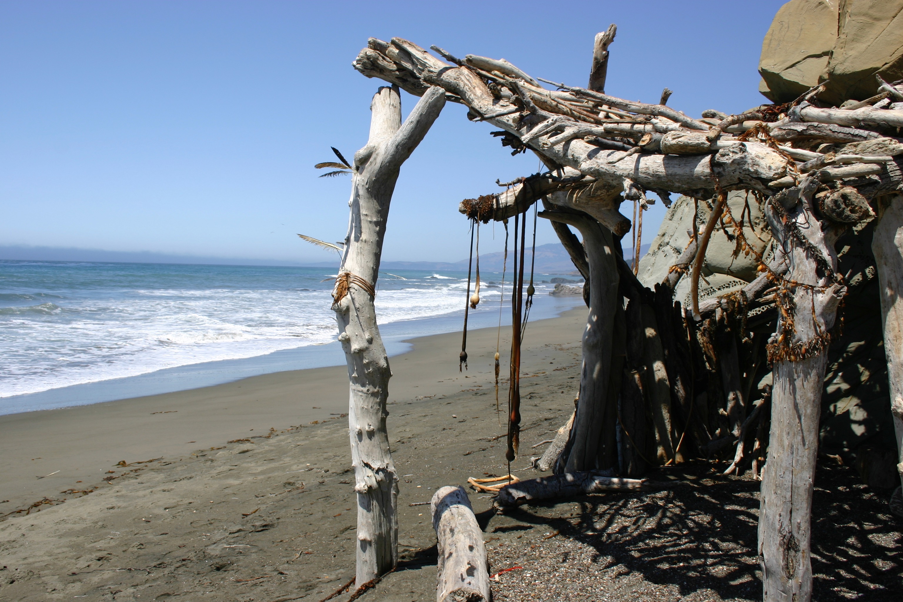 A hut constructed of driftwood and seaweed on the beach. 