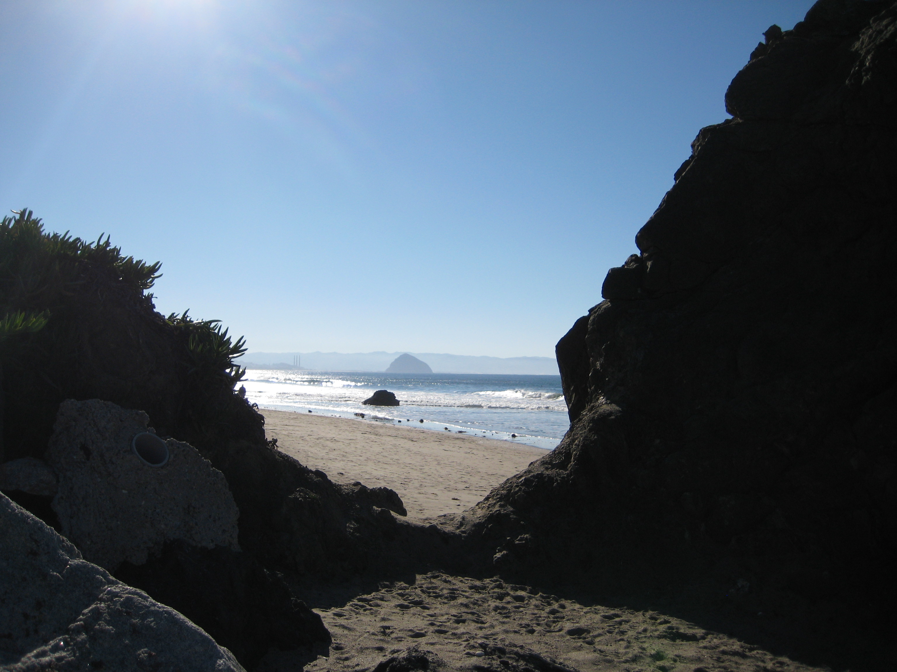 Rock formation on a beach landscape. Morro Rock centered in the distance. 
