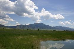 A pond reflects fluffy white clouds on a mountain-flanked plain in Idaho. 