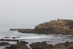 Two people standing in the distance on a rocky coastal outcropping, looking at the ocean.
