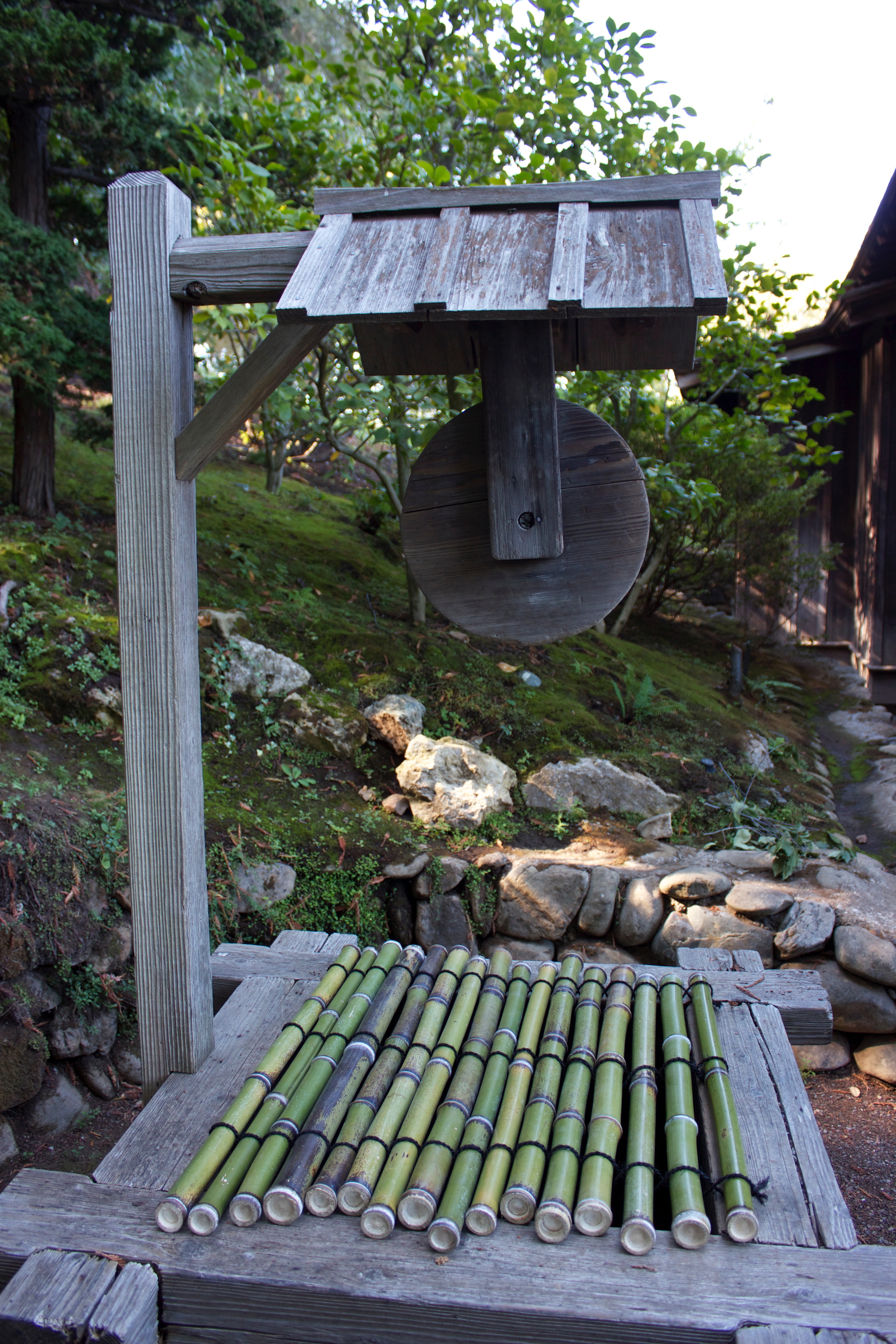 An old wooden water well in a Japanese garden, covered by bamboo stalks strung together. 