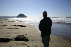 A man stands on the beach, gazing toward Morro Rock. 
