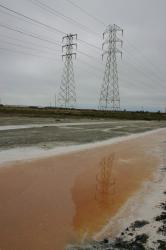 High voltage tower reflected in the water of a pink salt marsh.